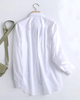 Long white rayon shirt with curved hem and pleated back displayed on wooden hanger

