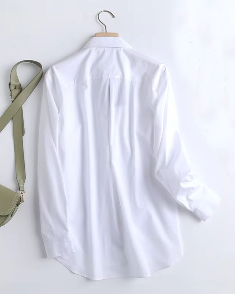 Long white rayon shirt with curved hem and pleated back displayed on wooden hanger

