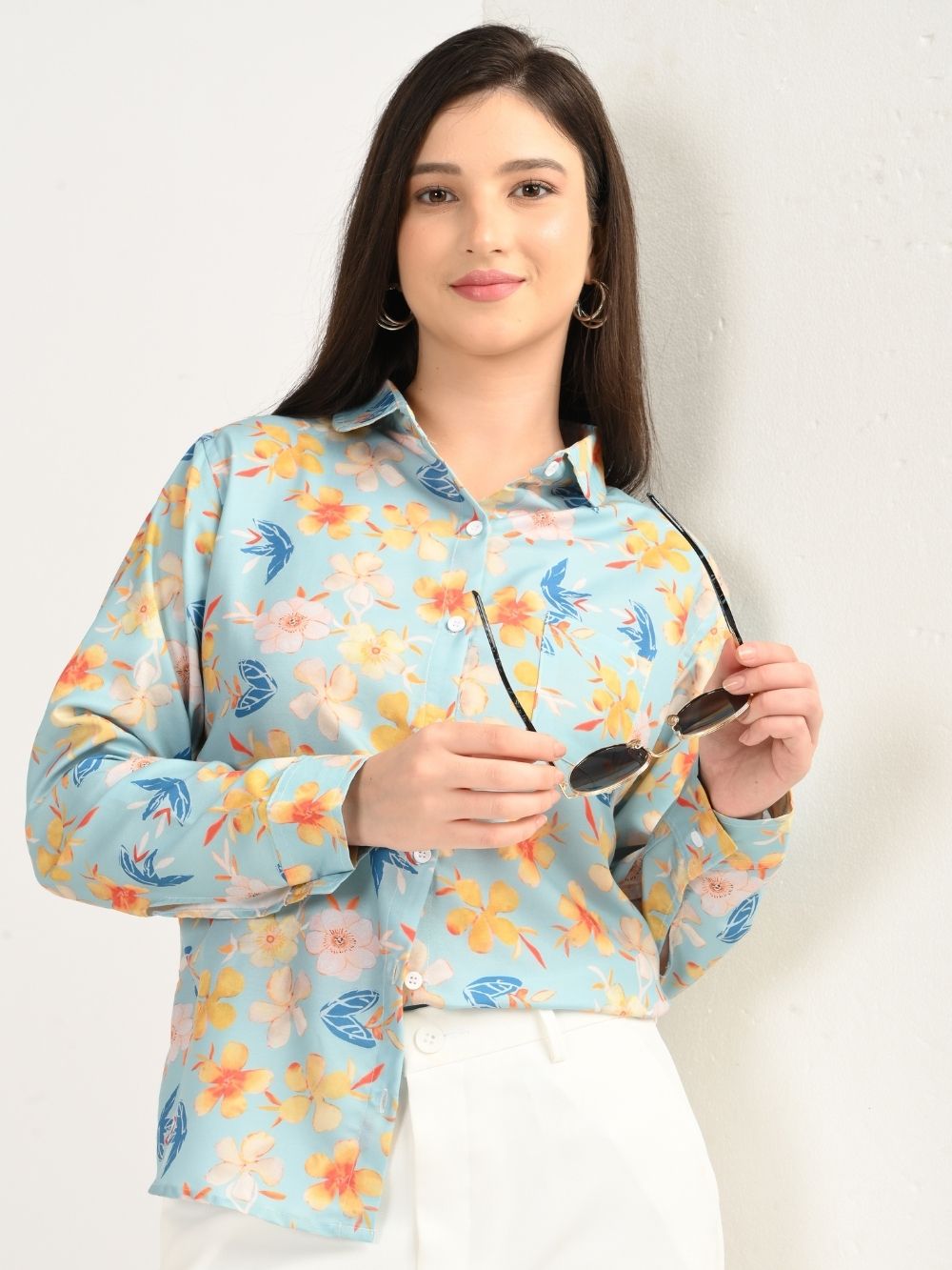 Woman holding sunglasses in aqua blue floral shirt, front view