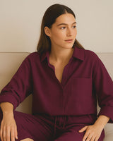“Woman wearing burgundy muslin cotton loungewear set, sitting comfortably on a couch”


