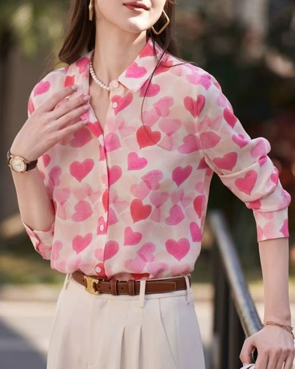 Woman wearing pink heart print blouse with white trousers, outdoors in natural light

